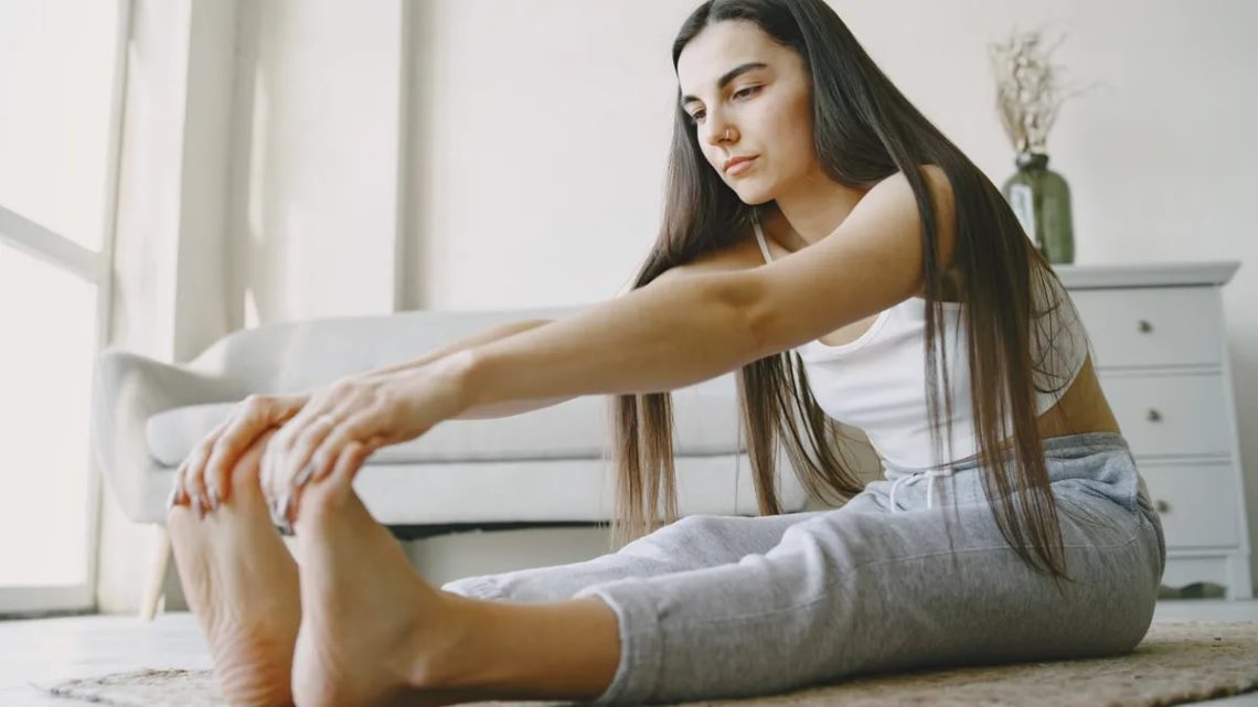 Young woman stretches on a rug in a light-filled room, embracing home fitness.